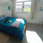 Bright double bedroom with large window, teal bed, and minimalist decor at Nordés Surfhouse in Ferrol Galicia
