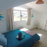 Cozy double room with sloped ceiling, wooden rack, and window views in Nordes Surfhouse Ferrol Galicia